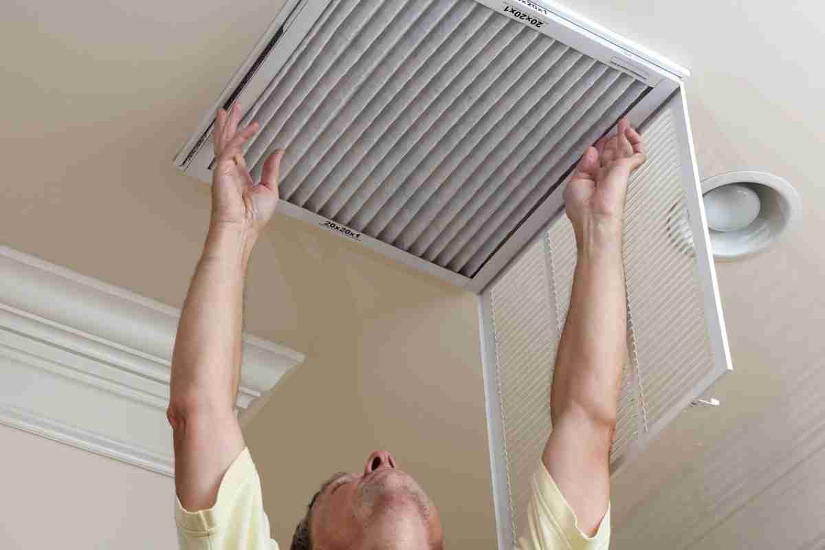 man installing new furnace filter in ceiling.