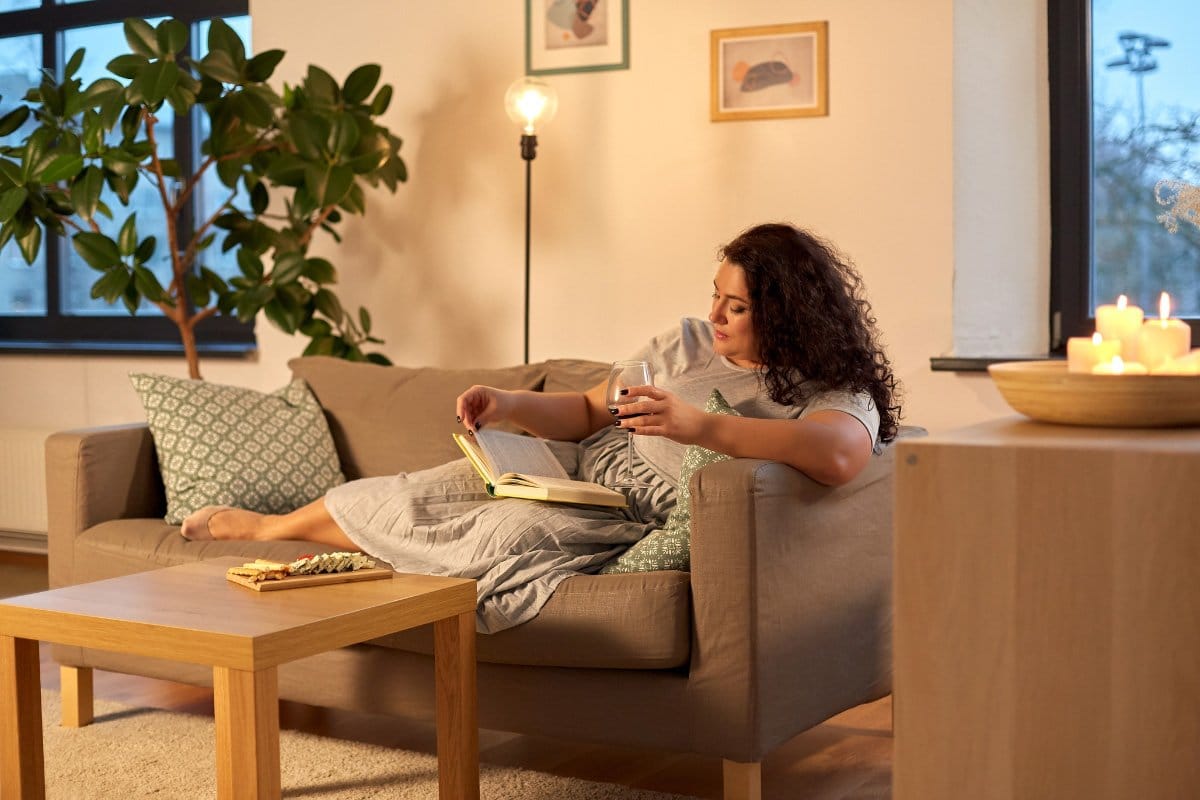 Woman relaxing on couch while reading abook and drinking a glass of wine.